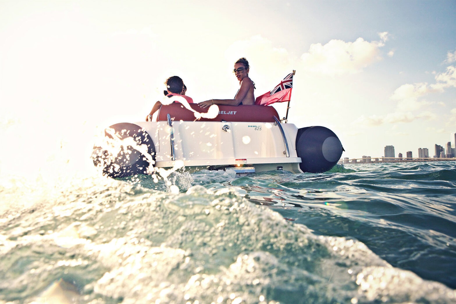 Two people on a Williams Jet Tender with a British flag, enjoying a sunny ride.