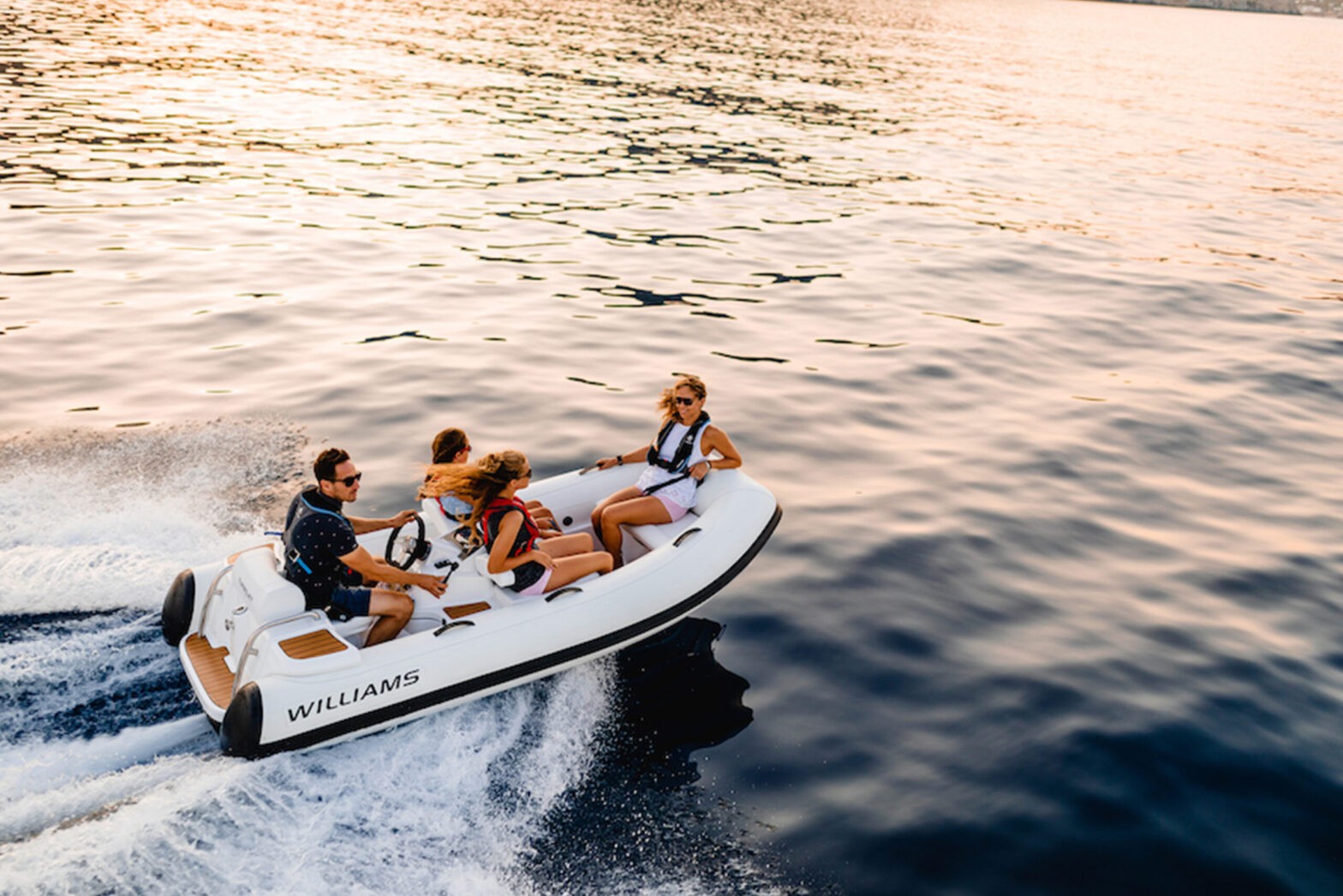 A group of people enjoying a ride on a Williams TurboJet 325, a small tender boat, during a beautiful sunset