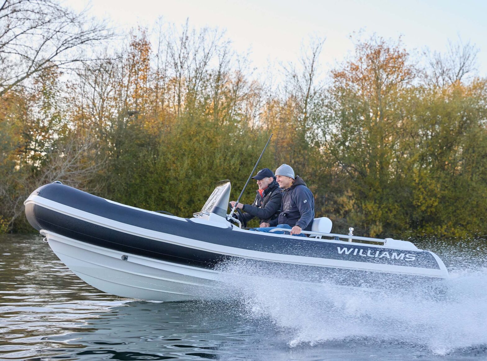 Two people enjoying a ride on a Williams Jet Tender, cruising past autumn trees.